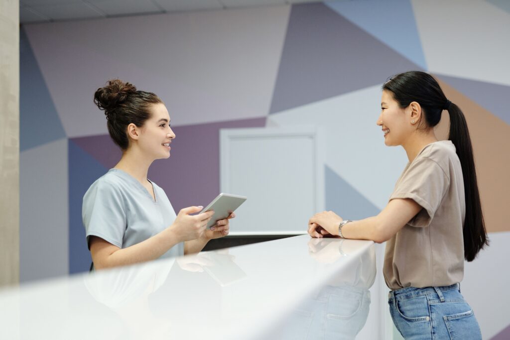 Receptionist and visitor speaking at a clinic reception desk