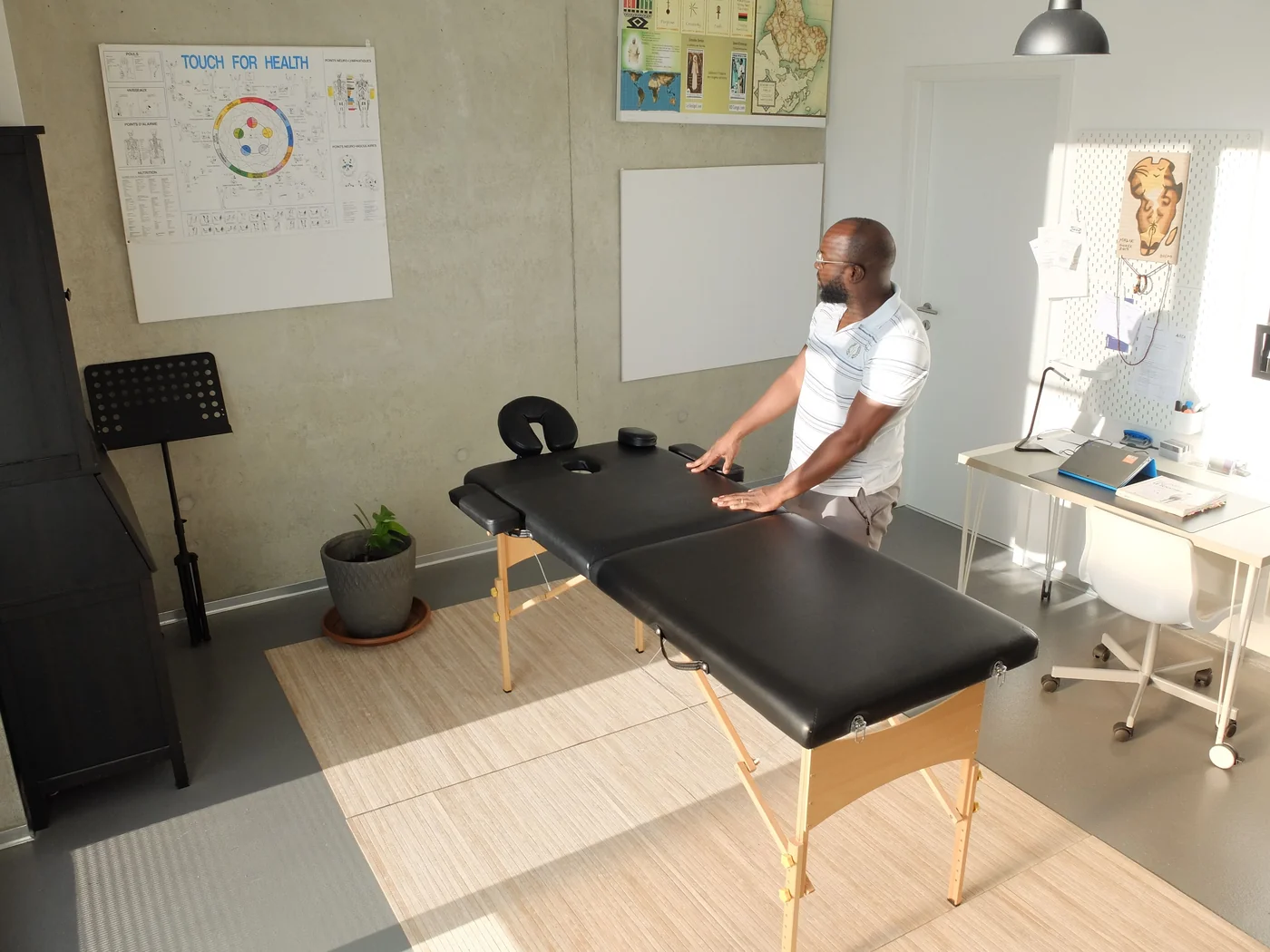 A practitioner stands beside a treatment table in a sunlit clinic room